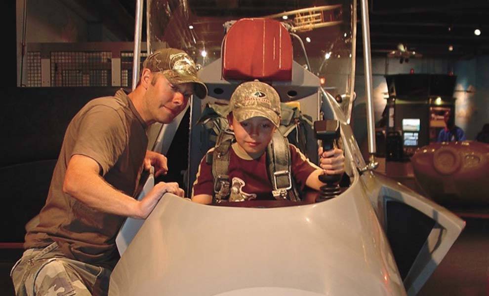 Un hombre y un niño sentados en la cabina de un avión de combate, mirando por la ventana con emoción