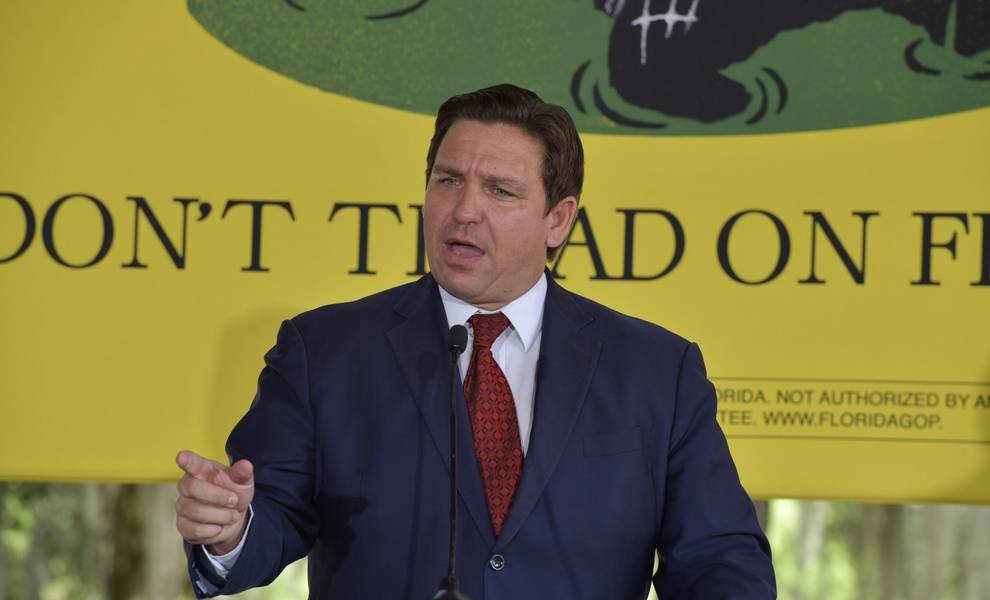 El gobernador Ron DeSantis, con traje y corbata, pronuncia un discurso en un podio.