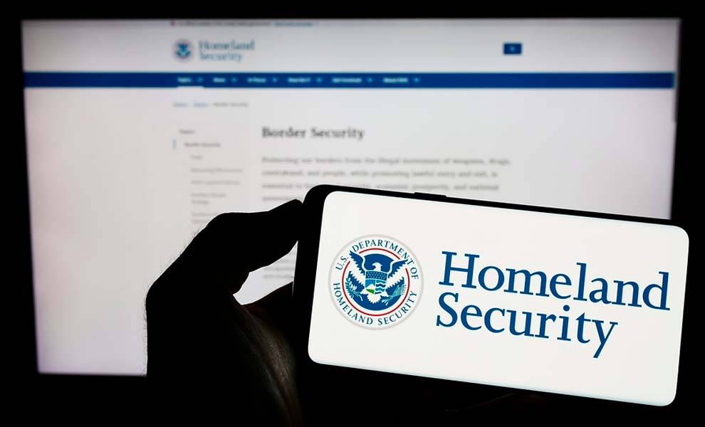 Persona que sostiene un teléfono celular con el Departamento de Seguridad Na-cional de EE. UU. en la pantalla.
