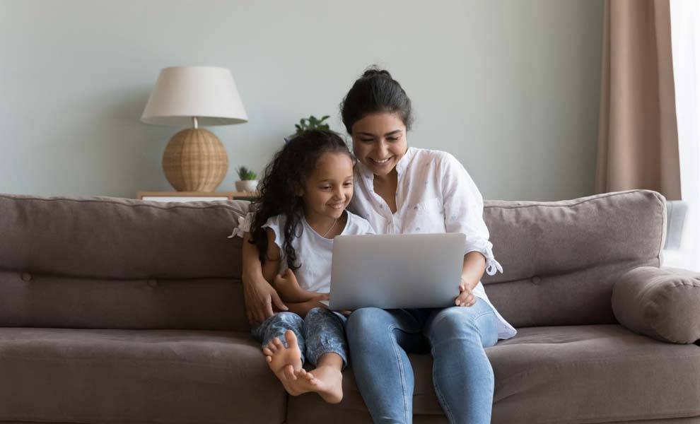 Una mujer y su hija están sentadas en un sofá mirando una computadora portátil.