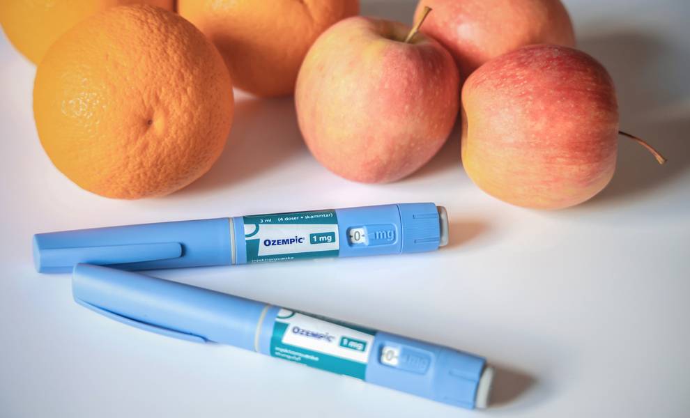 Dos inyectables de Ozempic sobre mesa con manzanas y naranjas.