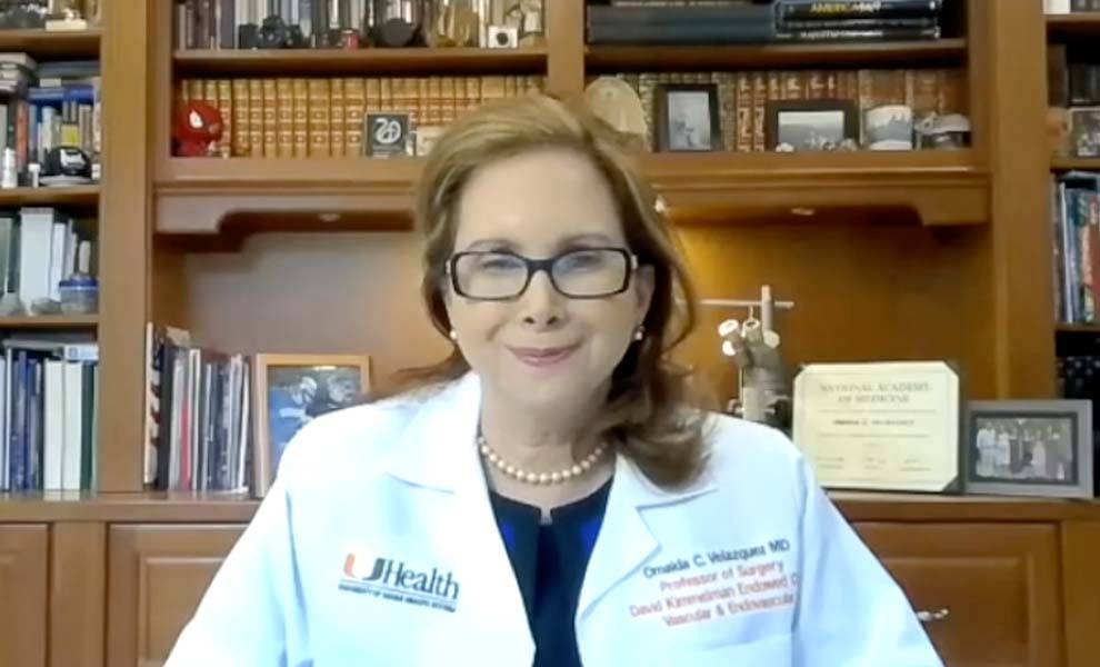 Dr. Omaida C. Velazquez in a lab coat is seated at a desk.