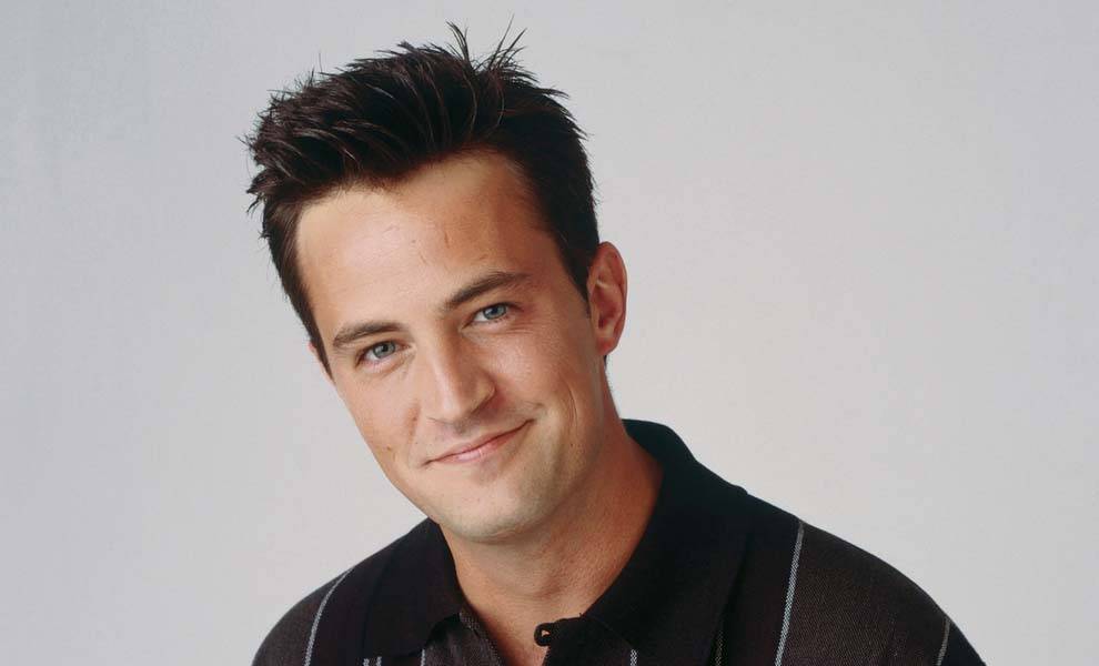 A man wearing a striped shirt smiles warmly at the camera, exuding a cheerful and friendly demeanor.