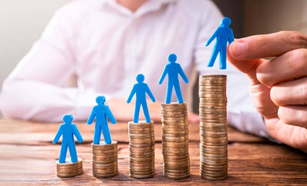 Una persona coloca cuidadosamente una figura azul sobre una pila de monedas, lo que simboliza el crecimiento financiero y la inversión.
