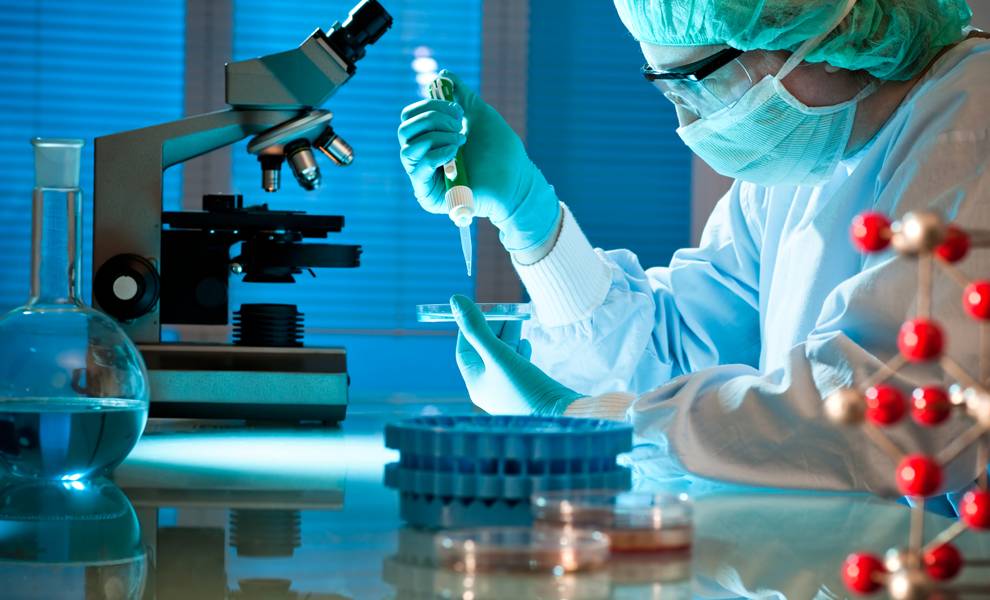 Un científico con bata de laboratorio examina una muestra bajo un microscopio en un entorno de laboratorio.