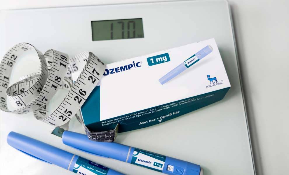 Weight loss drug Ozempic sitting on top of a scale with a measuring tape.