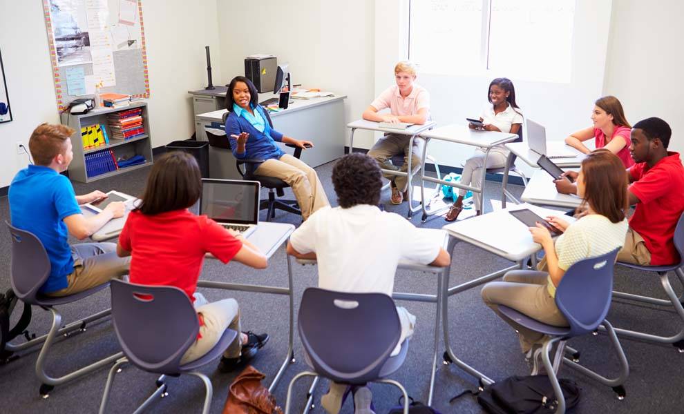A diverse group of students engaged in discussion while seated around a table in a classroom setting.