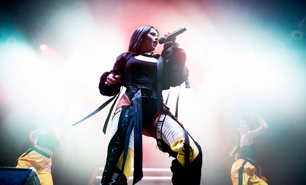 Becky G con un traje negro canta en el escenario.