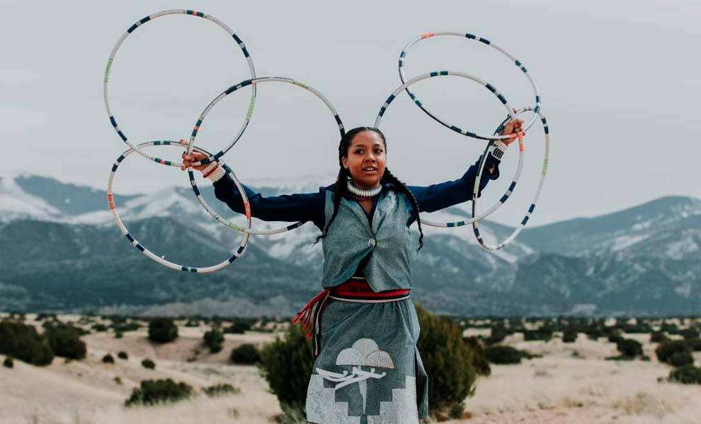 A woman in traditional attire holds up colorful hoops at the American Indigenous Arts Celebration in Big Cypress.