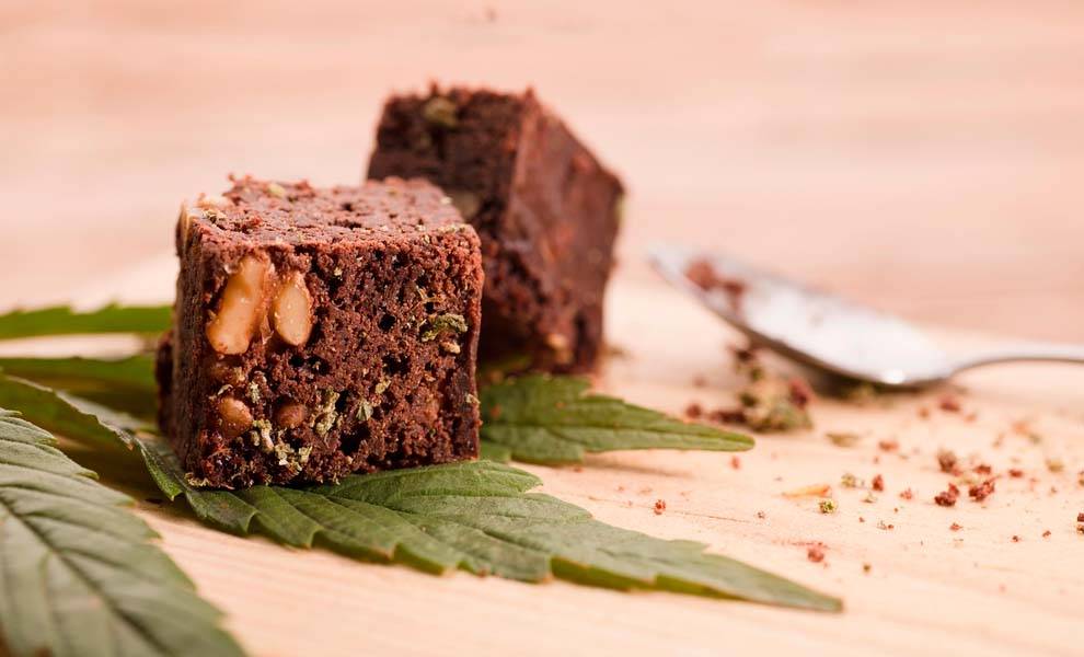 A plate of cannabis brownies garnished with fresh marijuana leaves.