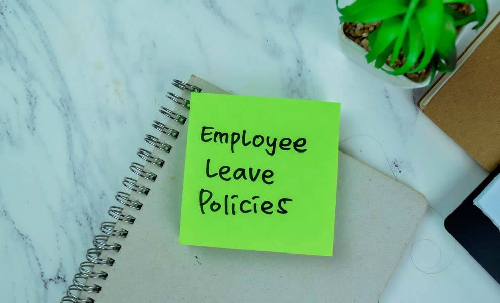 A plant and notebook on a table with a post it note that states employee leave policies.