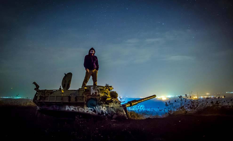 A man stands atop an old tank, silhouetted against the night sky.