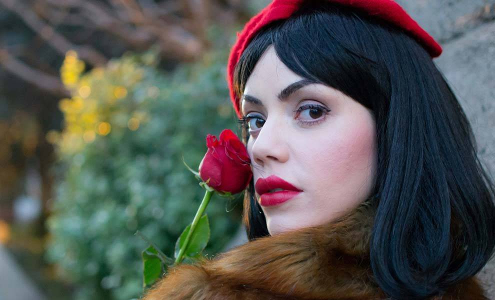 Una mujer con cabello negro y lápiz labial rojo sostiene con gracia una rosa vibrante.