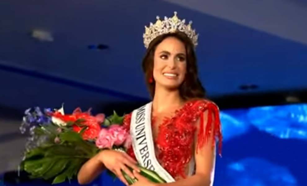 Marianela Ancheta, the woman representing Cubans in Miss Universe stands with a crown and red gown holding flowers.