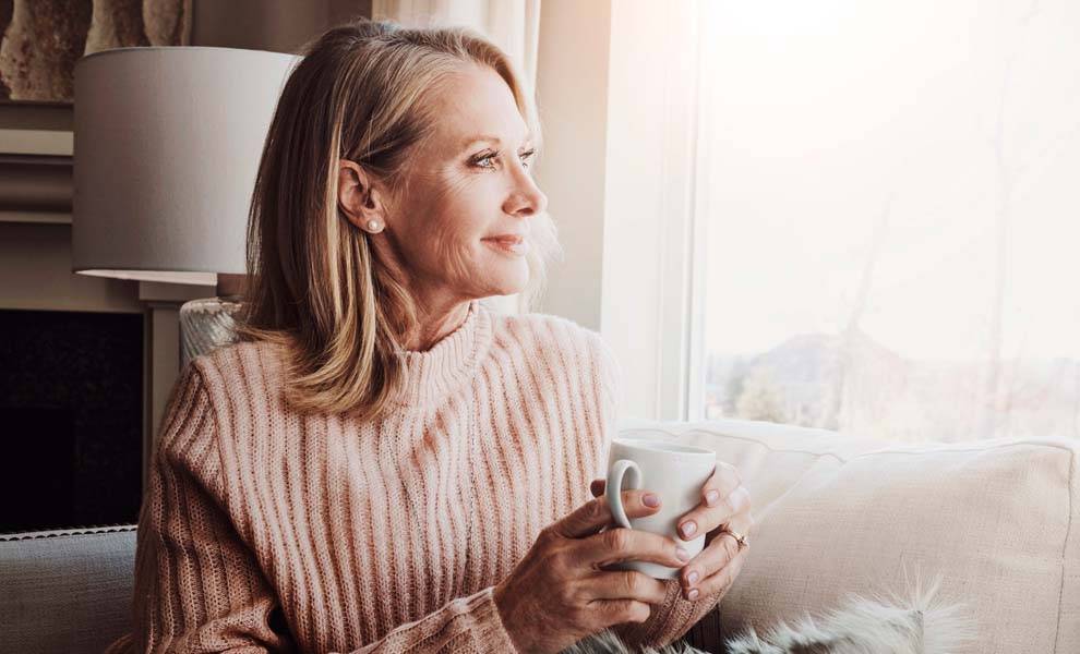 Una mujer sentada en un sofá, sosteniendo suavemente una taza de café en sus manos.