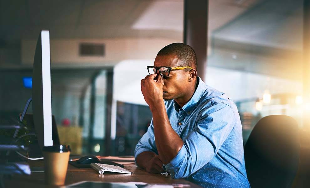 A man with his eyes closed sits at a desk, appearing contemplative or in deep thought.