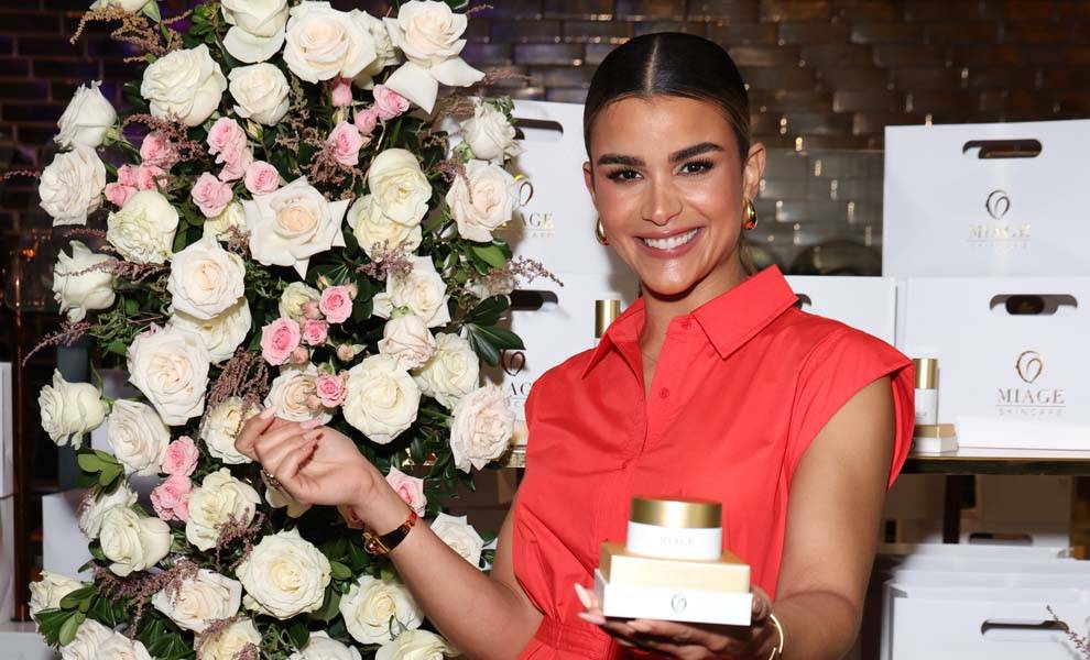 Una mujer sostiene un frasco de crema, rodeado de flores vibrantes, mostrando una mezcla de belleza y cuidado de la piel.