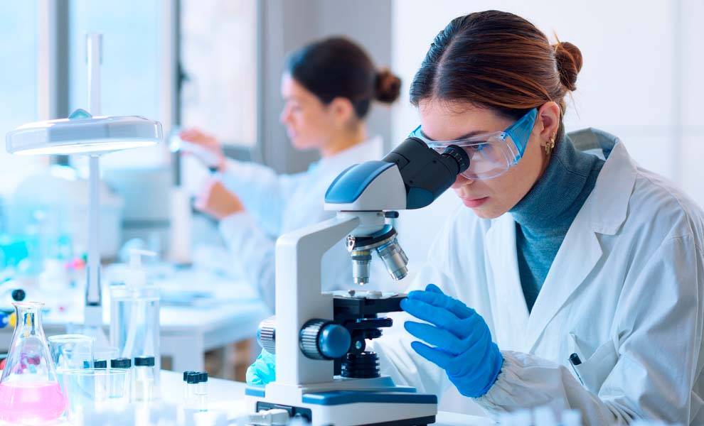 Una mujer con bata de laboratorio examina un microscopio, examinando un nuevo fármaco contra la obesidad.