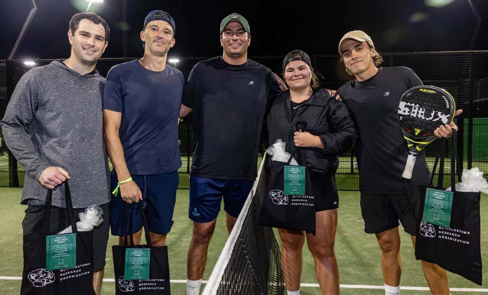 Cinco personas sonriendo y posando juntas en una cancha de tenis y Padel para un evento específico.