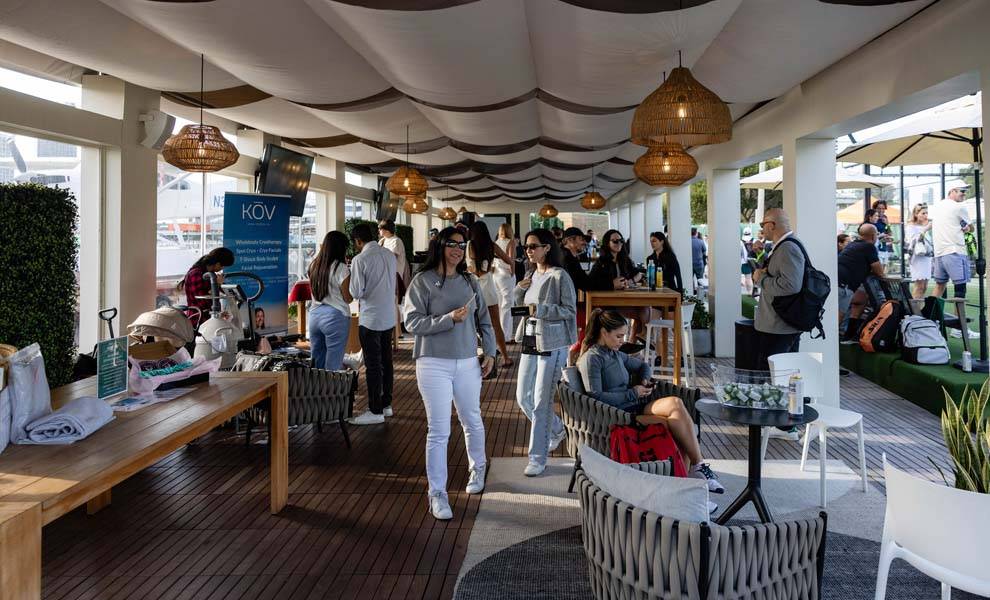 A group of people seated at tables and chairs in a shaded outdoor area at the Padel for a purpose event.