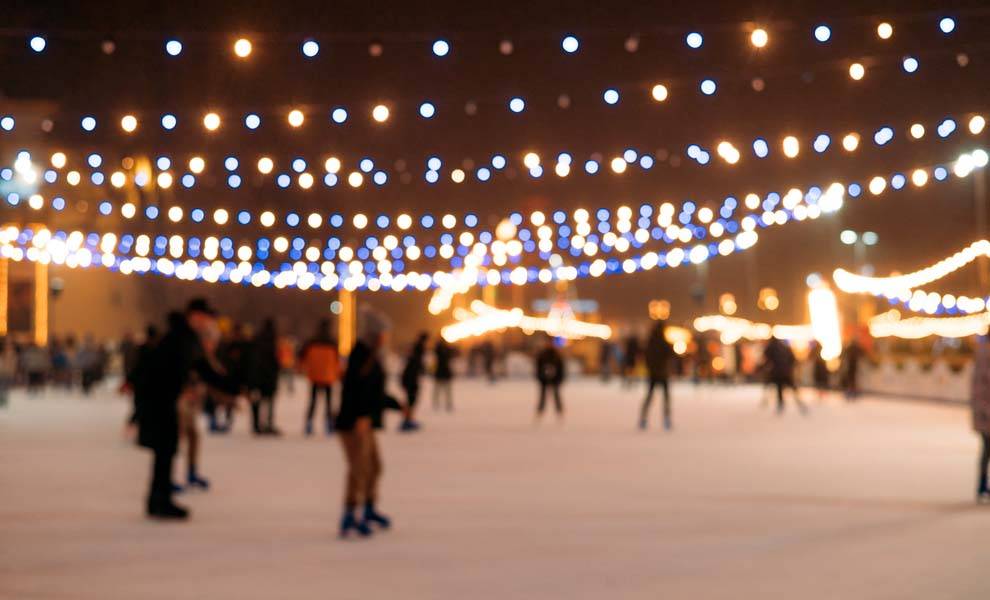 Un grupo de personas patinando sobre hielo en una pista de hielo iluminada por la noche, rodeada de luces festivas.