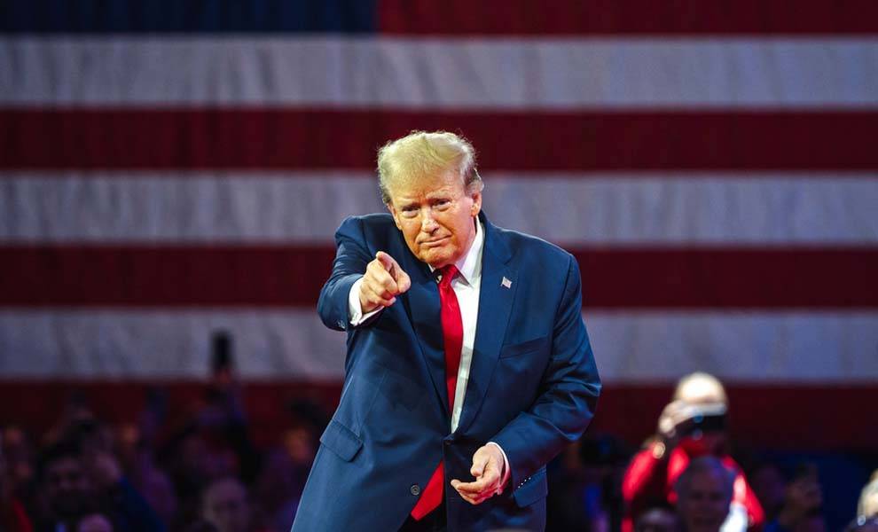 Donald Trump con un traje azul apuntando a la multitud.