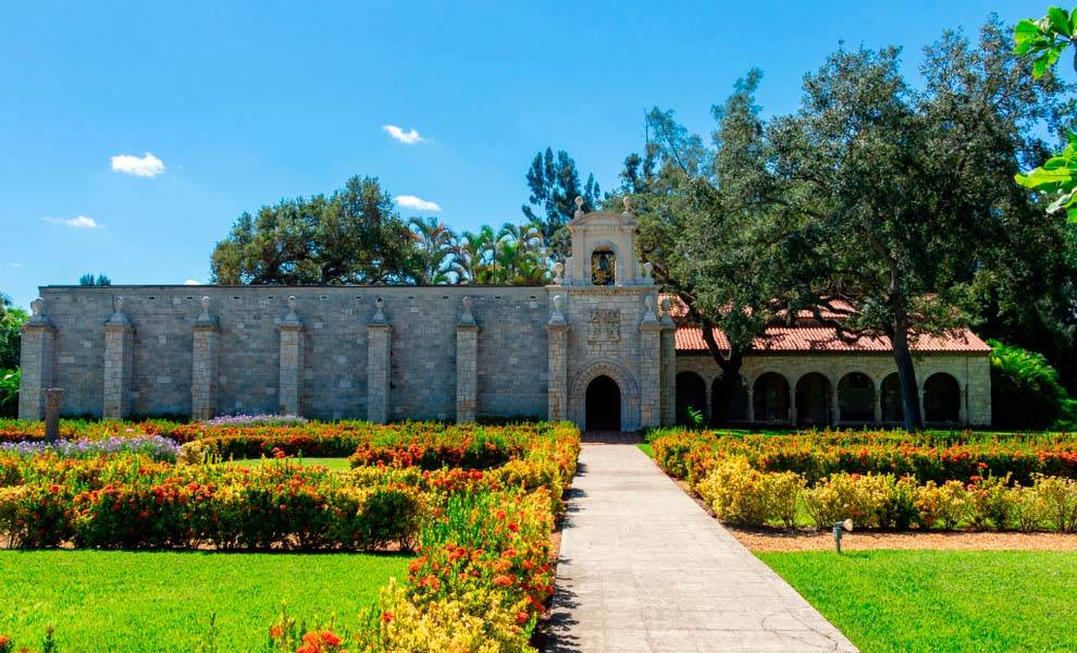 Un antiguo monasterio español en Miami rodeado de un exuberante jardín y árboles.