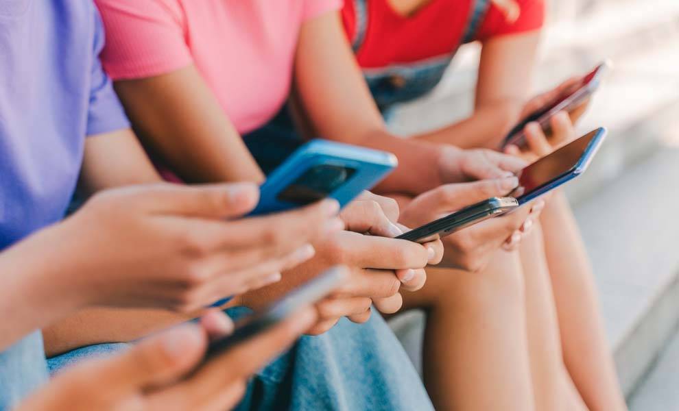 Un grupo diverso de menores sentados en escalones, cada uno de ellos interactuando con sus teléfonos inteligentes.