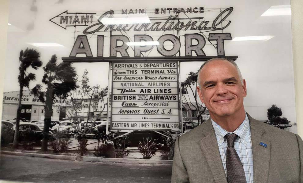 A man in a suit and tie stands confidently in front of a sign, exuding professionalism and poise.