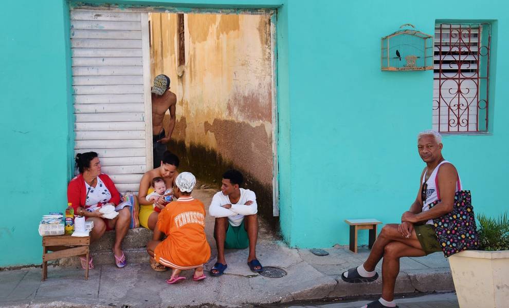 Un grupo de personas sentadas en la acera frente a un edificio azul en Cuba.