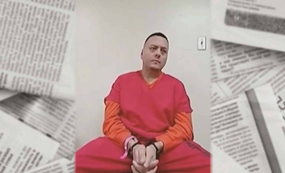 A man dressed in orange sits reading a newspaper, focused on the content in front of him.