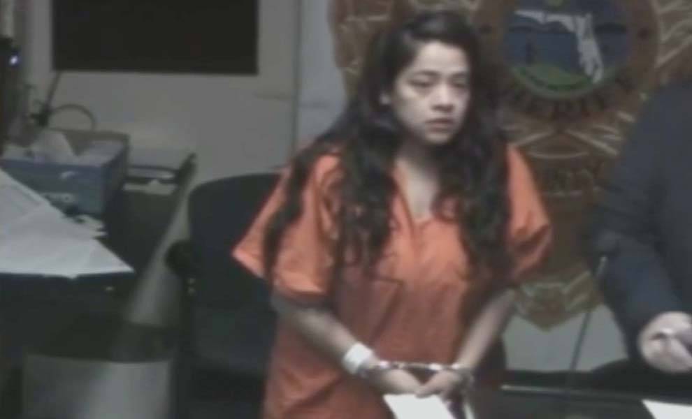 Naomi Ruiz in an orange shirt and handcuffs in a courtroom.
