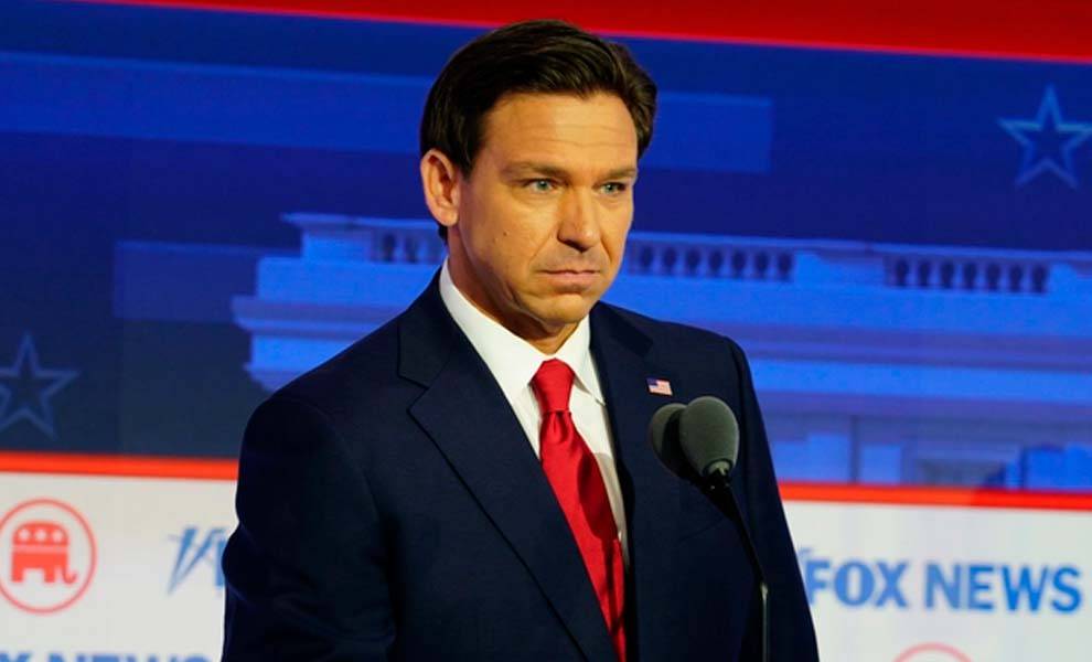 El gobernador de Florida, Ron DeSantis, con traje y corbata, se encuentra con confianza en un podio.