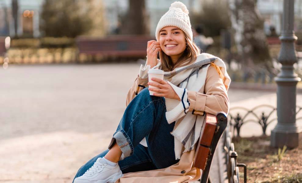 A woman wearing a beanie and coat sits on a bench, enjoying a moment of relaxation outdoors.