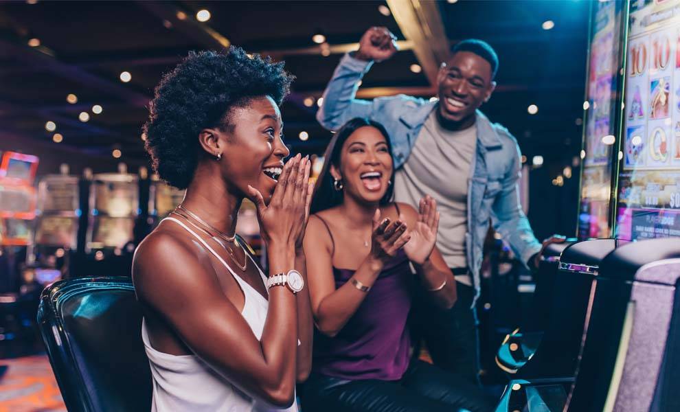Three individuals engaged in playing slot machines inside a vibrant casino environment.