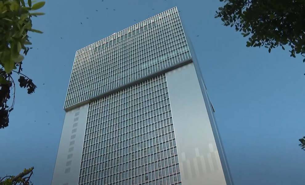 A tall building featuring a prominent large glass window reflecting the surrounding environment.