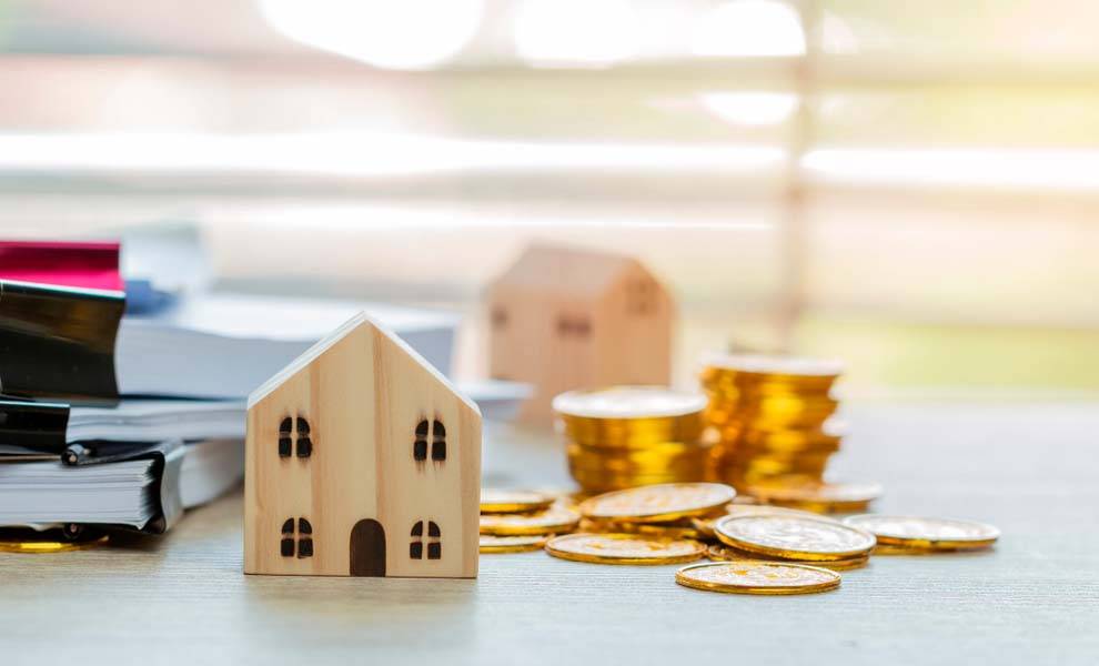 A house model and coins are placed on a desk, with a softly blurred background enhancing the focus on the items.