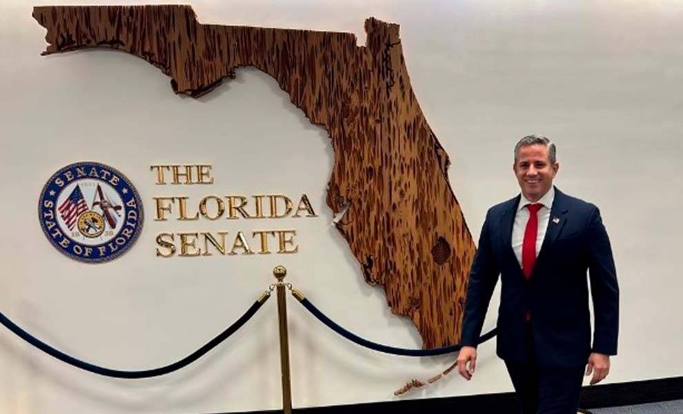Miami-Dade Tax Collector Dariel Fernandez stands in front of the Florida Senate Seal.