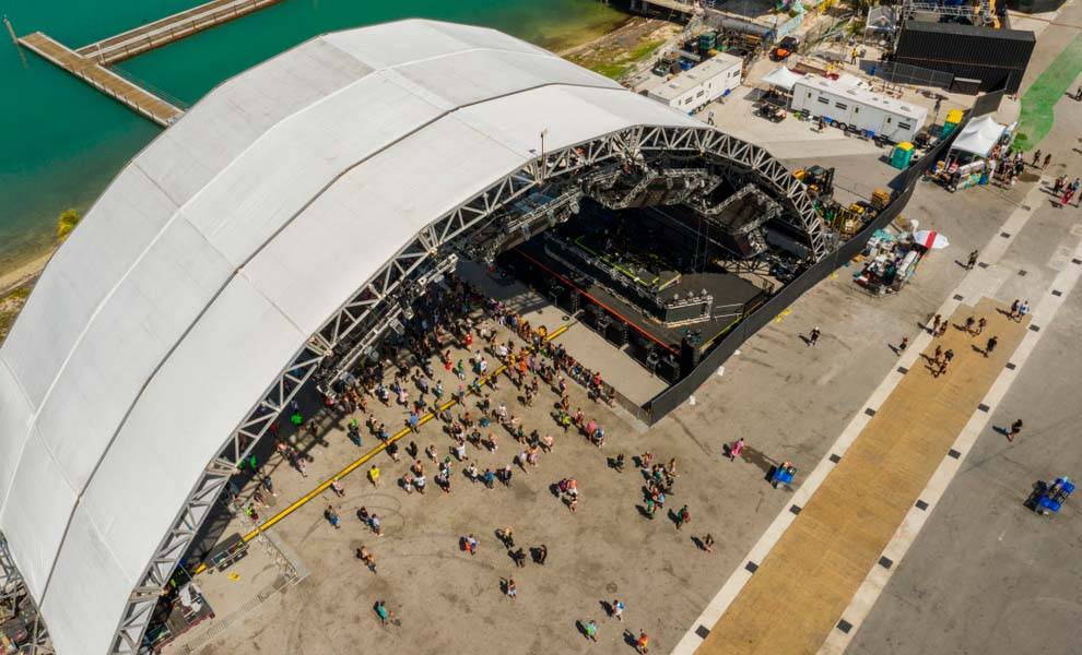 Aerial view of a large outdoor stage filled with people enjoying a live performance under a clear blue sky.