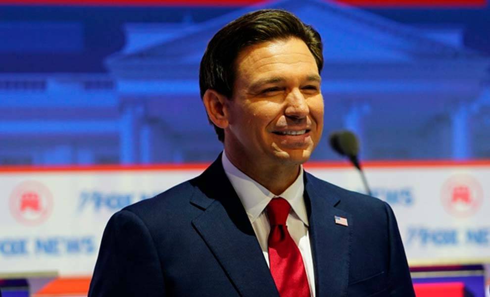 Florida Governor Ron Desantis in a suit and tie smiles confidently.