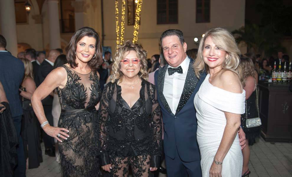 Un grupo de tres mujeres y un hombre sonriendo juntos para una foto en un evento social.