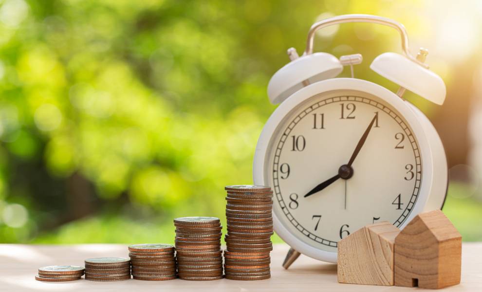 A clock beside stacks of coins on a table, symbolizing a time deadline and financial value.