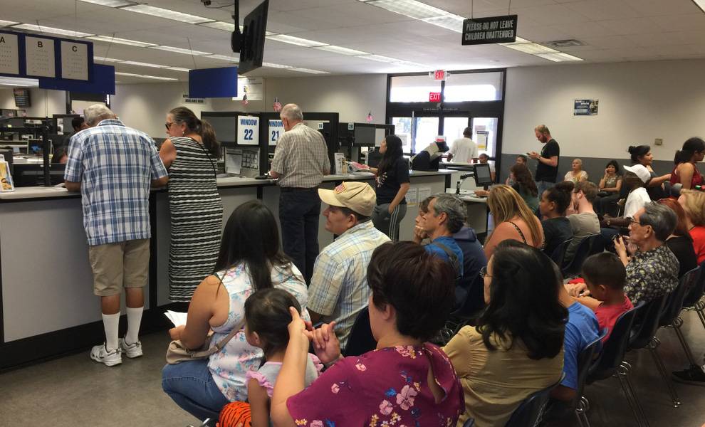 A line of people sitting at the DMV, waiting for their turn at the service counter.