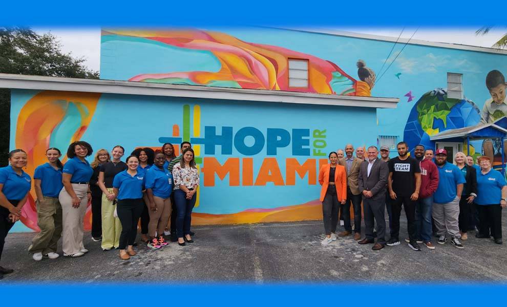 A diverse group of individuals stands before a vibrant mural displaying the words "Hope for Miami."