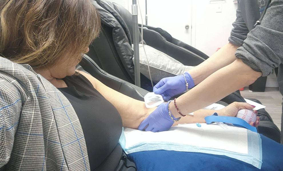 Rosi Rosell sentada en una silla de hospital mientras una enfermera le administra una vía intravenosa.