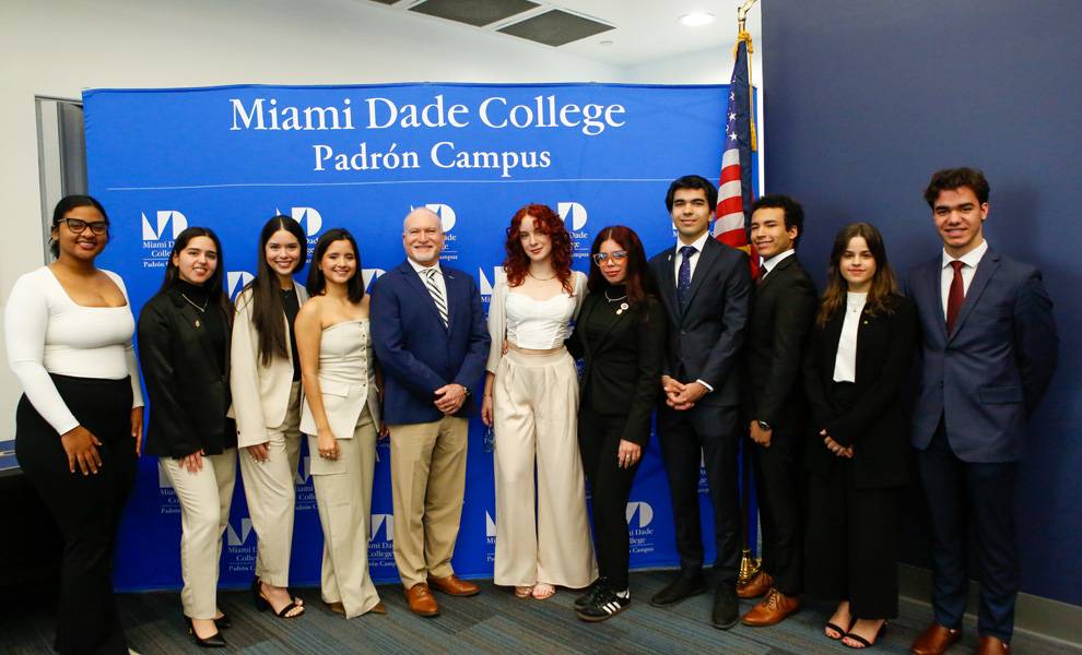 Un grupo de personas diversas sonriendo para una foto frente a un cartel del campus Padrón del Miami Dade College.