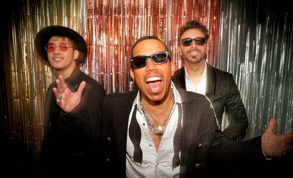 Dominican group Ilegales standing in front of a metallic background.