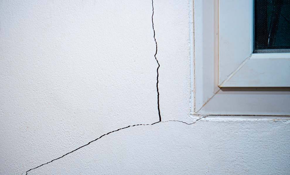A close-up view of a crack in the wall of a high-rise, featuring a window nearby, highlighting structural wear.