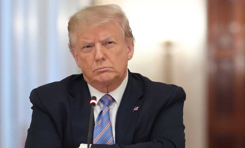 President Donald Trump at a podium in a black suit with a blue tie.