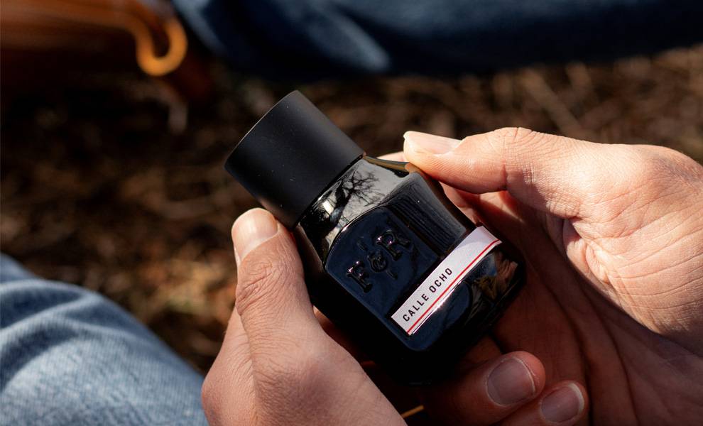 Una persona sostiene una botella en blanco y negro del perfume Calle Ocho, mostrando su elegante diseño y colores contrastantes.